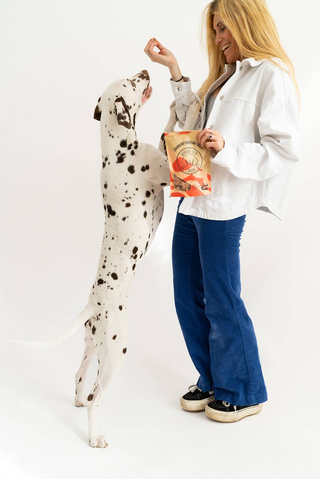 Person holding Winnie Lou’s Strawberry Shortcake dog biscuits while standing with a dog